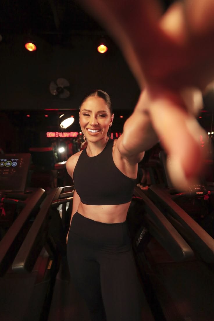 Woman smiling mid-workout in a dimly lit gym with warm red lighting